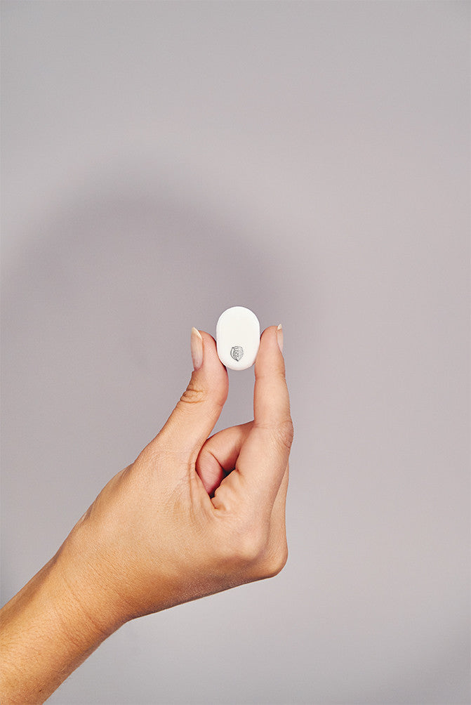 Hand holding a small white circular Ectosense sleep testing sensor against a grey background.
