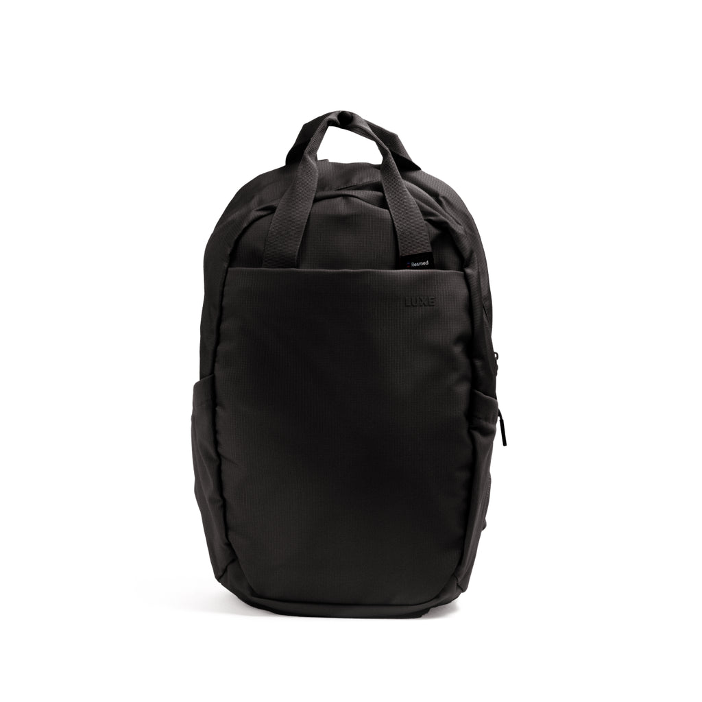 The Resmed Luxe, A black nylon backpack with dual top handles, a front slip pocket, and zippered side pockets, photographed against a solid white background.