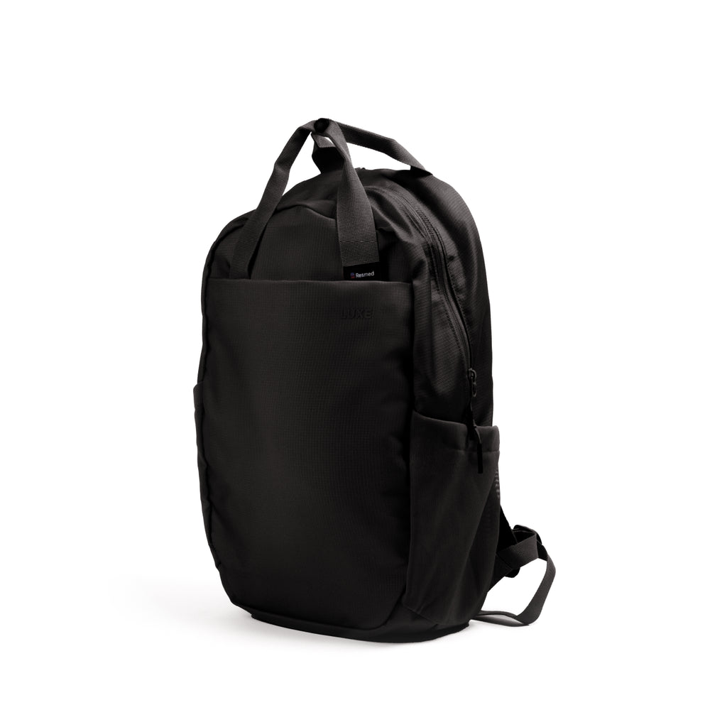Resmed Luxe bag, A black nylon backpack with top carry handles, a front zippered pocket, and side pockets, shown from a three-quarter angle on a white background.