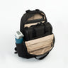 The Resmed Luxe, A black backpack with beige interior lining, shown open to display its compartments, pockets, and a side water bottle holder containing a blue water bottle, on a white studio background.