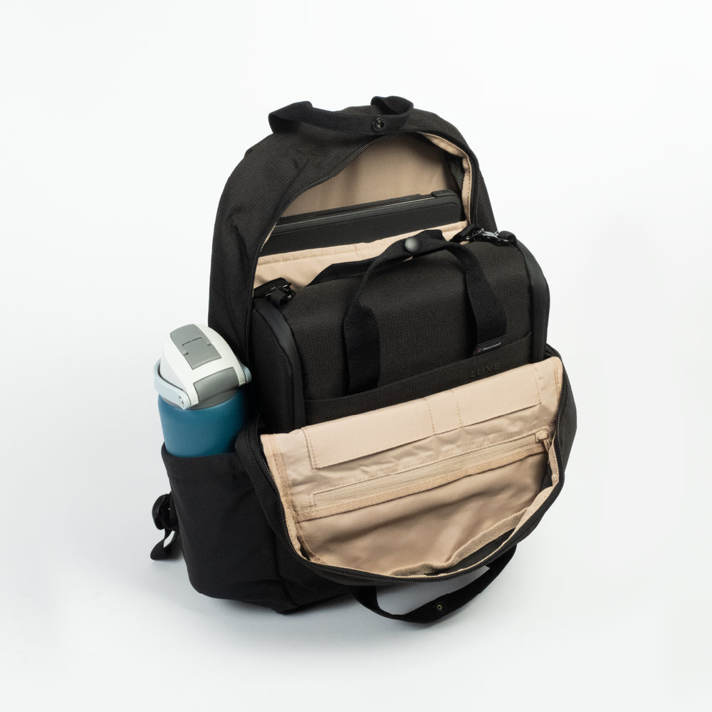 The Resmed Luxe, A black backpack with beige interior lining, shown open to display its compartments, pockets, and a side water bottle holder containing a blue water bottle, on a white studio background.