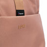 Close-up of a the Luxe tote dusty rose pink, showing the front pocket with the embossed brand name LUXE and a black Resmed logo tag on a beige webbing strap.
