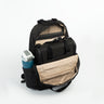 A black backpack shown open with a CPAP insert, on a white studio background, with beige interior lining and a side pocket holding a blue water bottle. 
