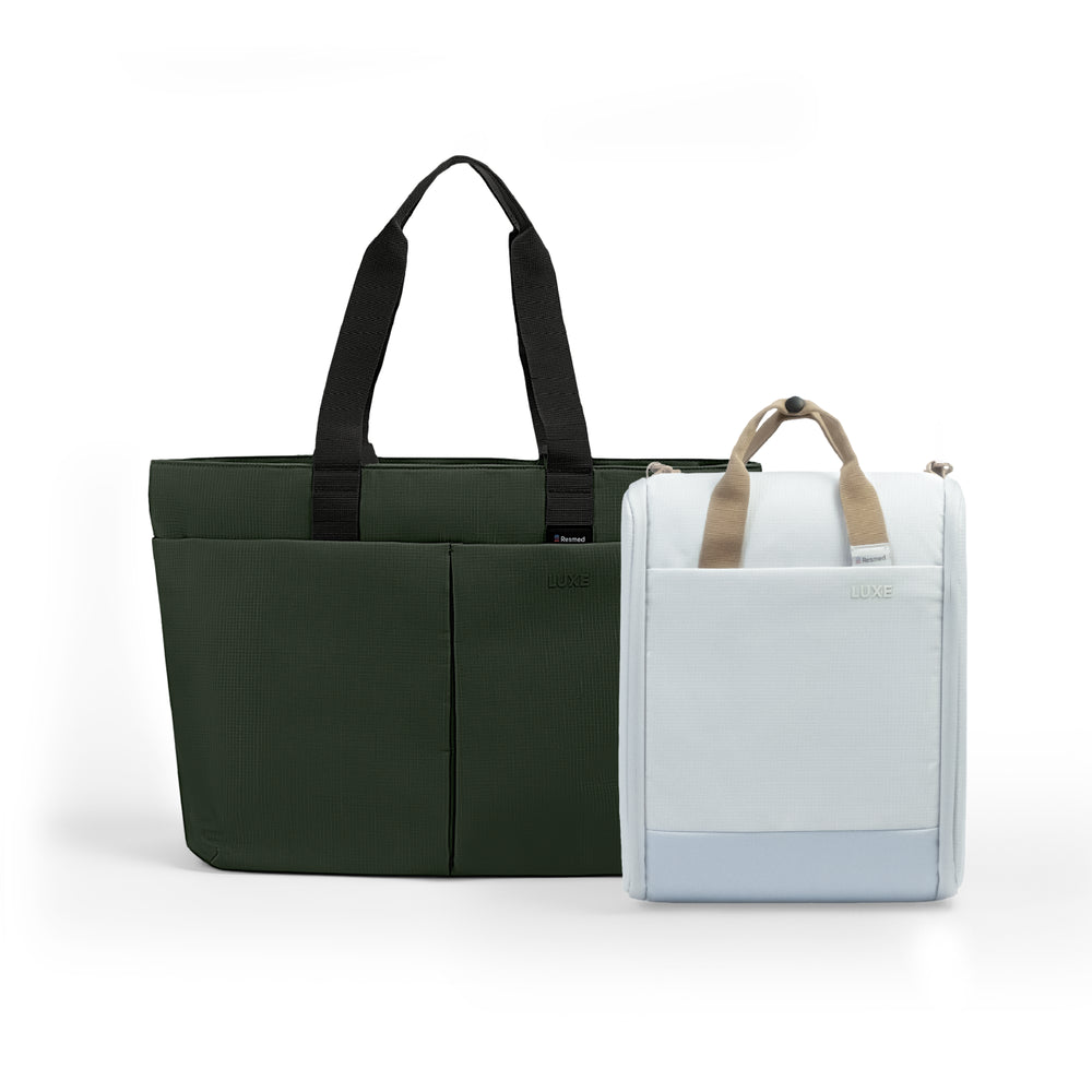A green tote luxe bag and a white cpap insert bag next to each other. The larger bag is dark green with black handles and front seam detailing.