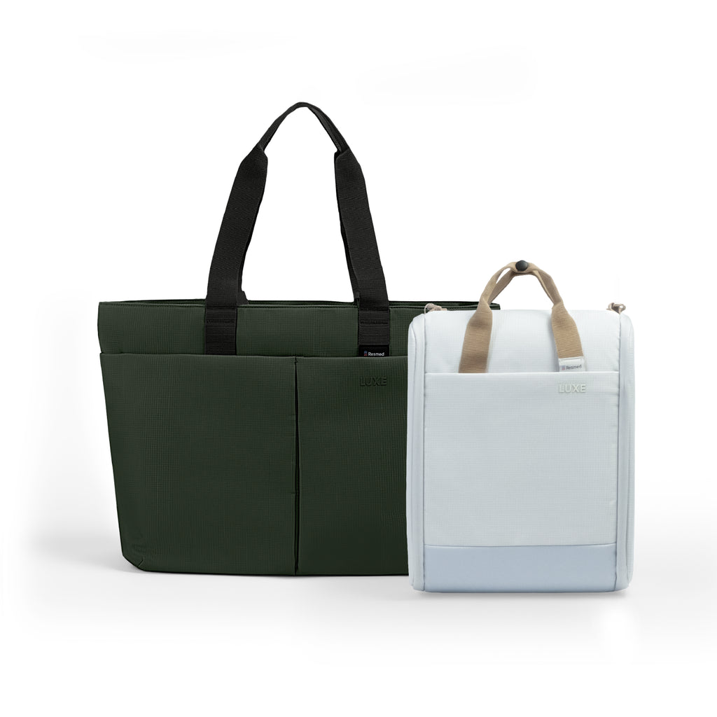A green tote luxe bag and a white cpap insert bag next to each other. The larger bag is dark green with black handles and front seam detailing.