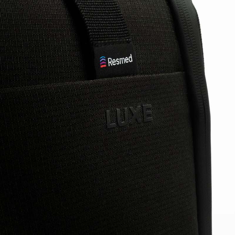 Close-up of a black CPAP insert with a visible Resmed logo patch on the strap and embossed LUXE branding on the front pocket.