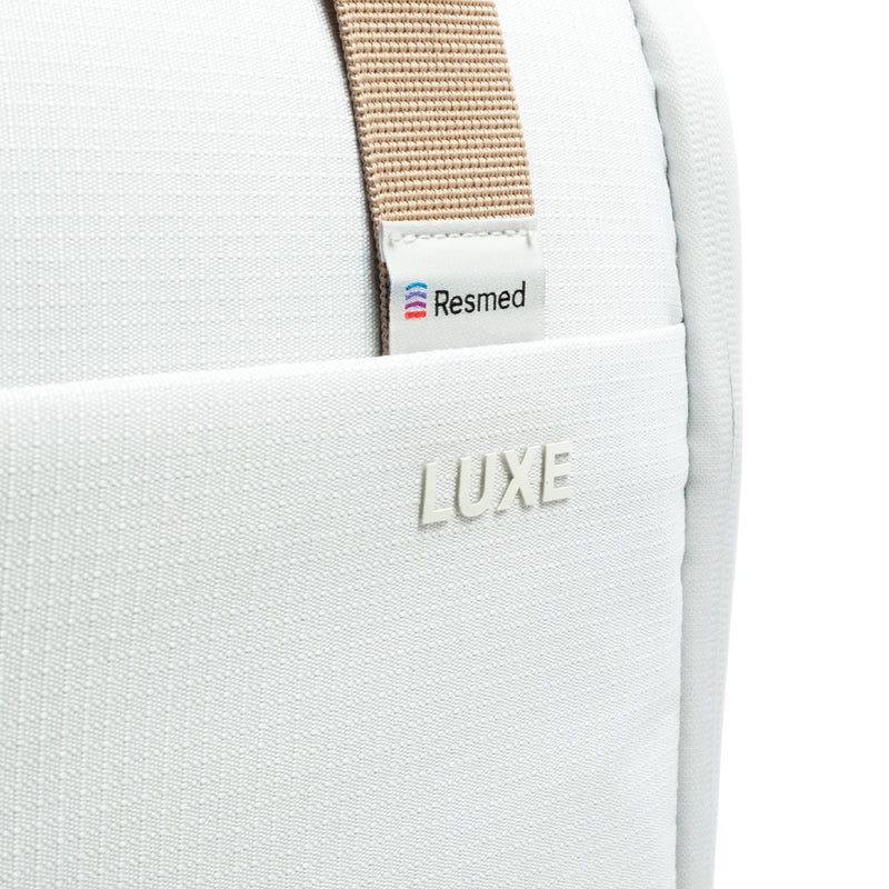 Close-up of the CPAP insert bag with a beige webbing strap and a small white Resmed label, plus an embossed LUXE logo on the front pocket.