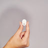 Hand holding a small white circular Ectosense sleep testing sensor against a grey background.